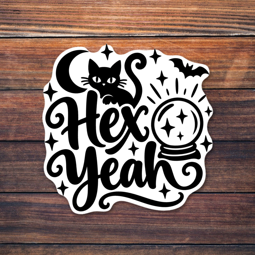 Black cat sitting on swirly script lettering that reads Hex Yeah, with a crescent moon, a glowing crystal ball, a bat and sparkle stars. shown on a wooden table