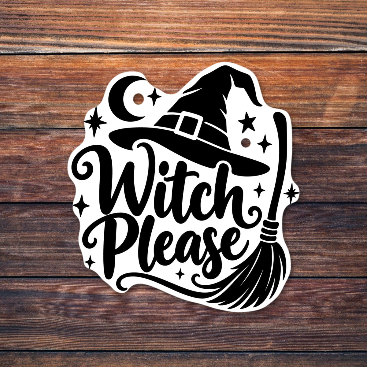 Black witch hat with a buckle above swirly script text reading Witch Please, with a broomstick, crescent moon, stars and sparkles shown on a wooden table
